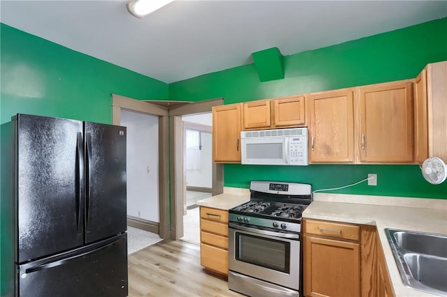 kitchen with black fridge, sink, stainless steel range with gas stovetop, and light wood-type flooring