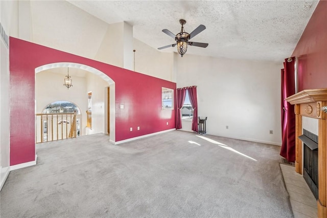 unfurnished living room featuring a tile fireplace, ceiling fan with notable chandelier, high vaulted ceiling, carpet floors, and a textured ceiling