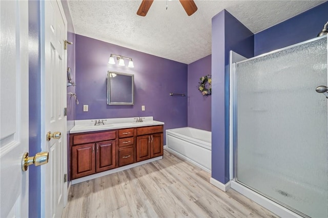 bathroom featuring independent shower and bath, wood-type flooring, vanity, ceiling fan, and a textured ceiling