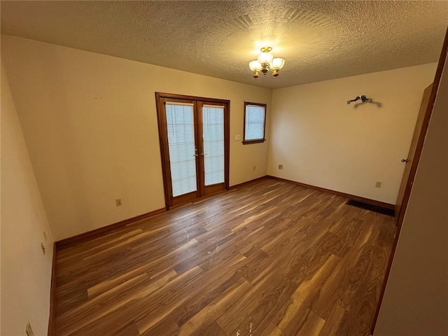 unfurnished room featuring dark hardwood / wood-style floors, an inviting chandelier, a textured ceiling, and french doors