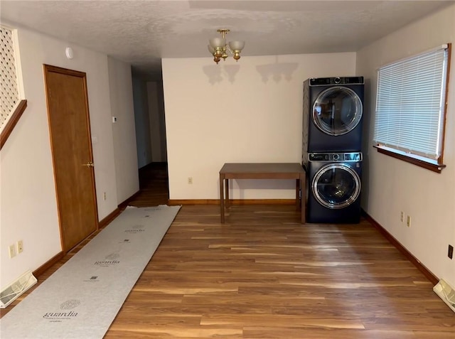 laundry room with a notable chandelier, baseboards, stacked washer / dryer, visible vents, and wood finished floors