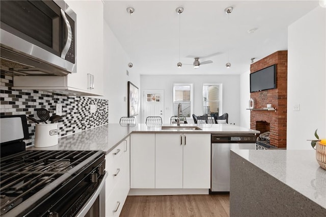 kitchen with pendant lighting, sink, stainless steel appliances, white cabinets, and kitchen peninsula