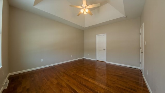 unfurnished room with dark wood-type flooring, ceiling fan, and a tray ceiling