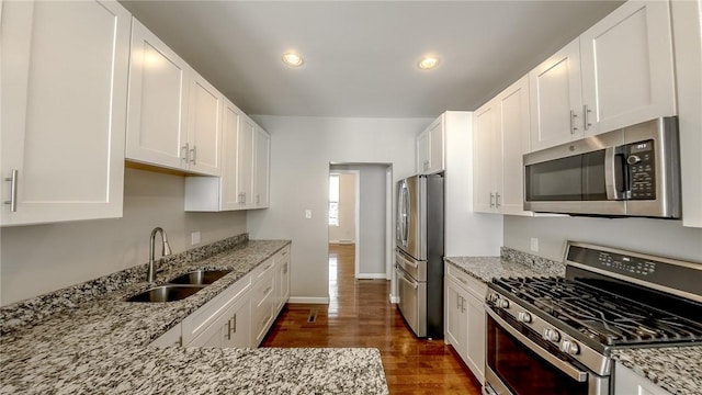 kitchen featuring stainless steel appliances, white cabinetry, light stone countertops, and sink