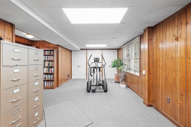 exercise area with wooden walls, light carpet, and a drop ceiling