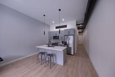 kitchen with sink, appliances with stainless steel finishes, a kitchen breakfast bar, pendant lighting, and a kitchen island with sink