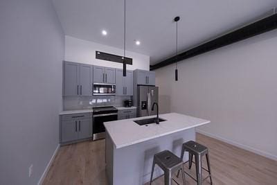 kitchen featuring sink, gray cabinets, appliances with stainless steel finishes, a center island with sink, and decorative light fixtures