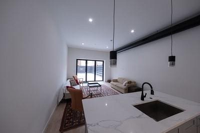 kitchen with wood-type flooring, light stone countertops, sink, and pendant lighting