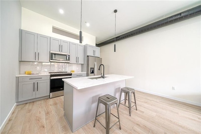 kitchen with an island with sink, sink, gray cabinetry, a kitchen bar, and stainless steel appliances