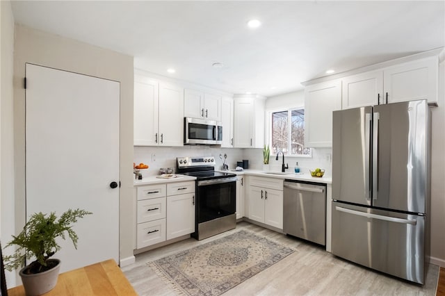 kitchen featuring sink, white cabinetry, tasteful backsplash, light hardwood / wood-style flooring, and stainless steel appliances