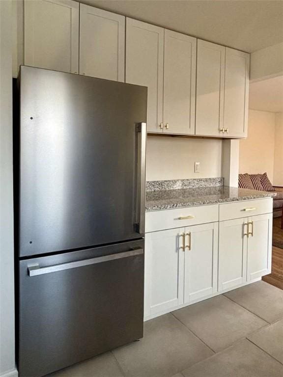 kitchen featuring stainless steel refrigerator, light stone counters, and white cabinets