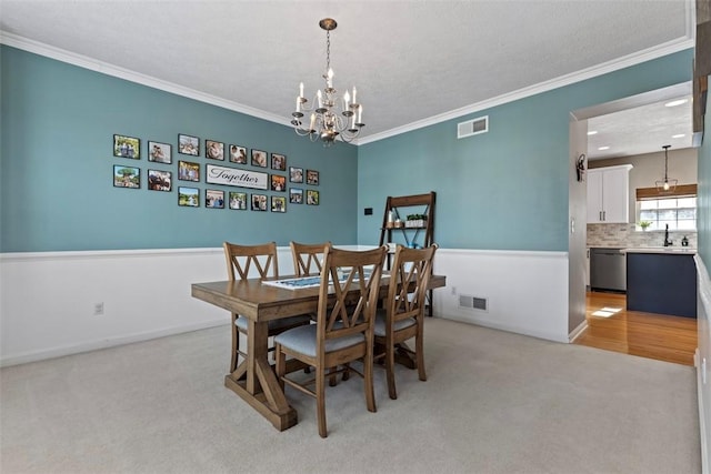 dining space featuring sink, a chandelier, light colored carpet, crown molding, and a textured ceiling