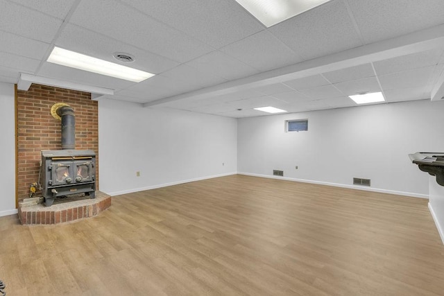 unfurnished living room with a wood stove, a paneled ceiling, and light hardwood / wood-style floors