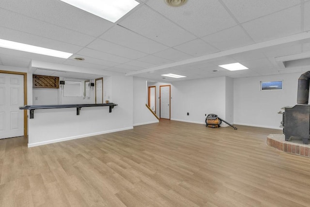 basement featuring a drop ceiling, light hardwood / wood-style floors, and a wood stove