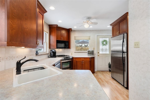 kitchen with sink, light wood-type flooring, appliances with stainless steel finishes, ceiling fan, and backsplash