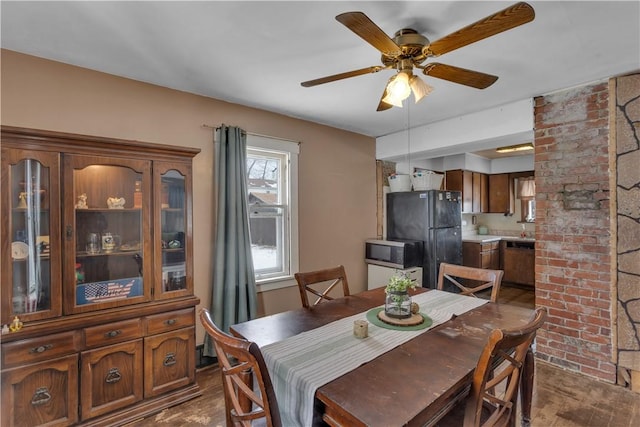 dining area with brick wall, dark wood-type flooring, and ceiling fan