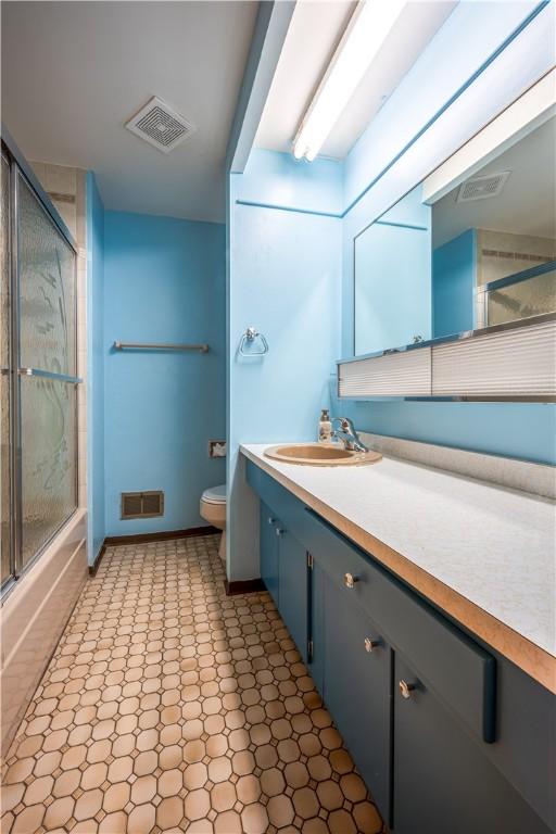 full bathroom featuring vanity, bath / shower combo with glass door, and toilet