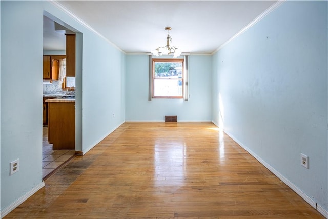 unfurnished dining area with an inviting chandelier, crown molding, and light hardwood / wood-style floors