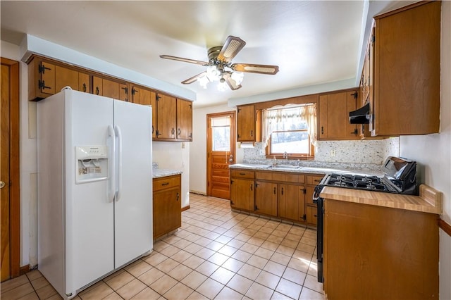 kitchen featuring ventilation hood, sink, white refrigerator with ice dispenser, ceiling fan, and gas range