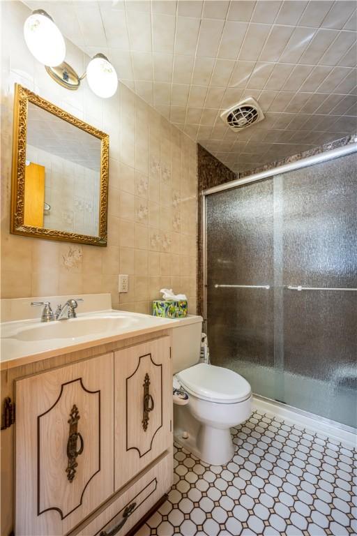 bathroom featuring an enclosed shower, vanity, toilet, and tile walls