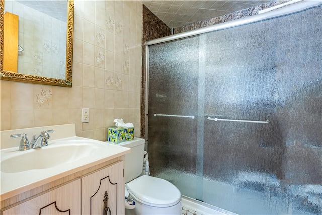 bathroom with vanity, toilet, a shower with door, and tile walls