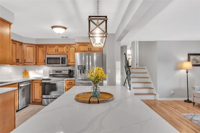 kitchen with light stone counters, hanging light fixtures, and appliances with stainless steel finishes