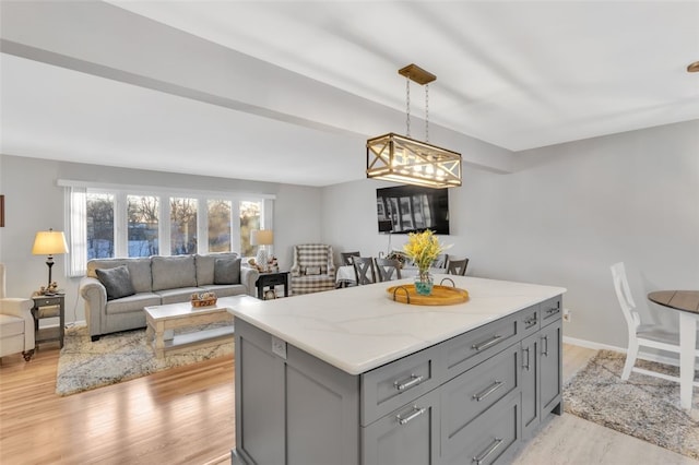 kitchen with pendant lighting, light hardwood / wood-style flooring, gray cabinets, a center island, and light stone counters