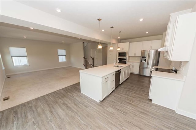 kitchen with decorative light fixtures, light hardwood / wood-style flooring, a center island with sink, appliances with stainless steel finishes, and white cabinets