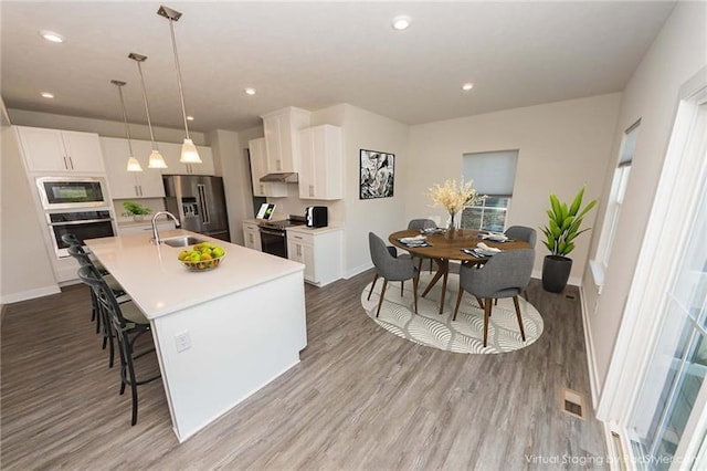 kitchen with white cabinetry, sink, hanging light fixtures, black appliances, and a center island with sink