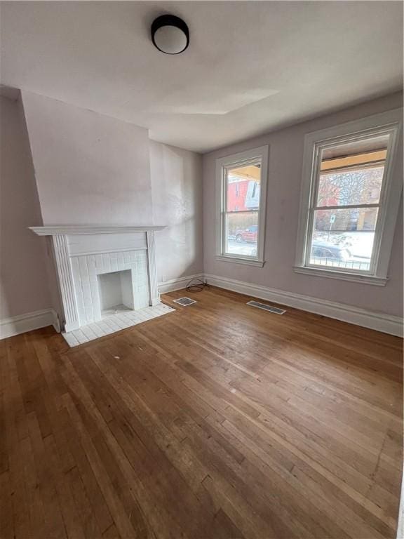 unfurnished living room with a tiled fireplace, a wealth of natural light, and light hardwood / wood-style floors