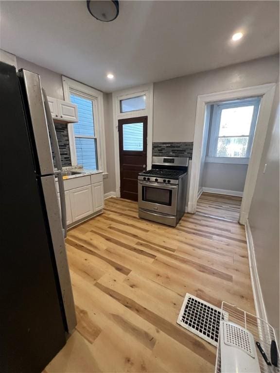 kitchen featuring appliances with stainless steel finishes, white cabinets, light wood-type flooring, and decorative backsplash