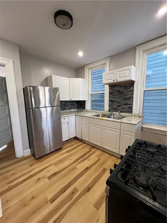 kitchen featuring sink, stainless steel fridge, white cabinetry, light hardwood / wood-style floors, and black range with gas stovetop