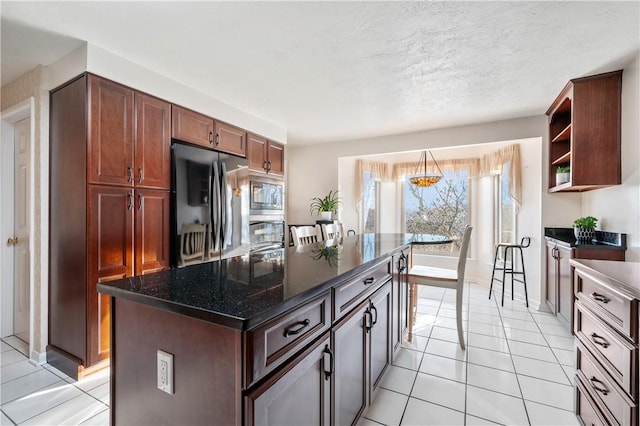 kitchen with stainless steel microwave, a kitchen island, light tile patterned flooring, and black fridge