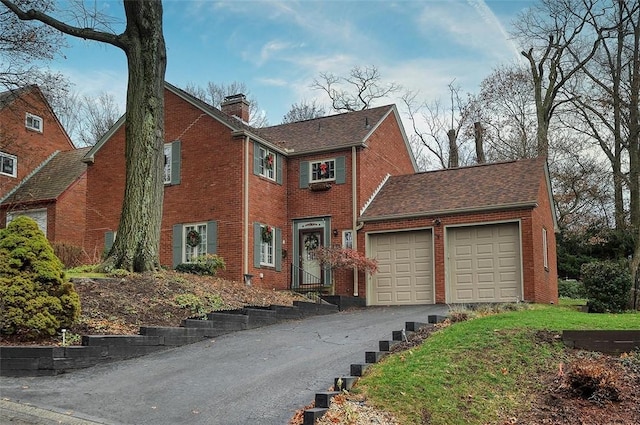 colonial home with a garage, brick siding, a chimney, and driveway