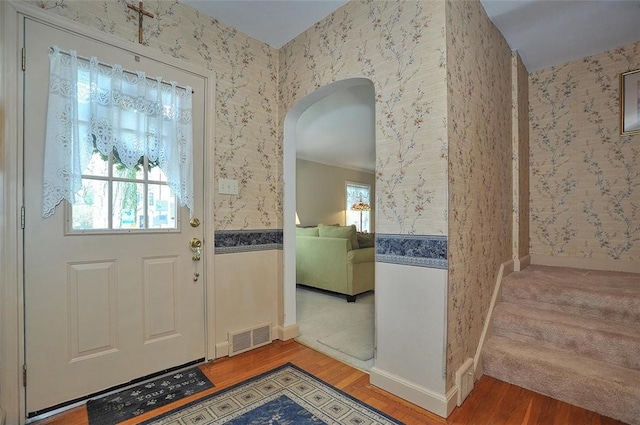 entryway with visible vents, arched walkways, wood finished floors, and wallpapered walls