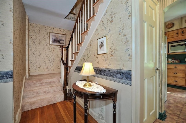 stairs with wood finished floors and wallpapered walls