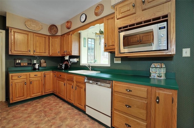 kitchen with dark countertops, wallpapered walls, white dishwasher, a sink, and stainless steel microwave