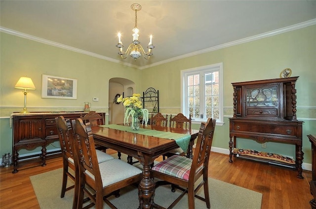 dining space with arched walkways, ornamental molding, an inviting chandelier, and wood finished floors