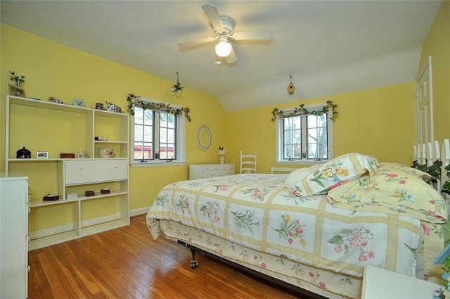 bedroom with vaulted ceiling, multiple windows, a ceiling fan, and wood finished floors