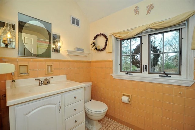 full bathroom featuring visible vents, toilet, vanity, lofted ceiling, and tile walls