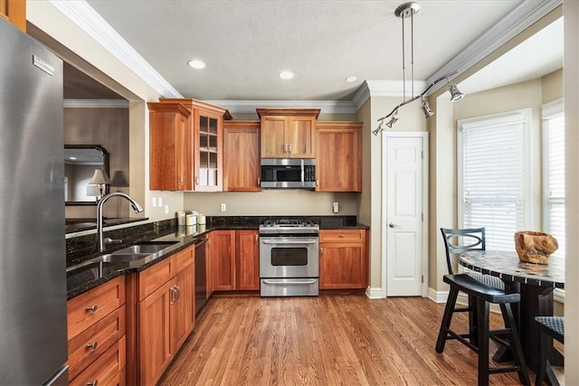 kitchen with pendant lighting, sink, appliances with stainless steel finishes, ornamental molding, and dark stone counters