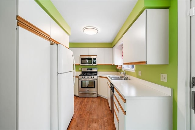 kitchen featuring stainless steel appliances, sink, white cabinets, and light wood-type flooring