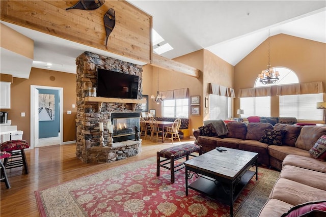 living room with high vaulted ceiling, a stone fireplace, hardwood / wood-style floors, and an inviting chandelier