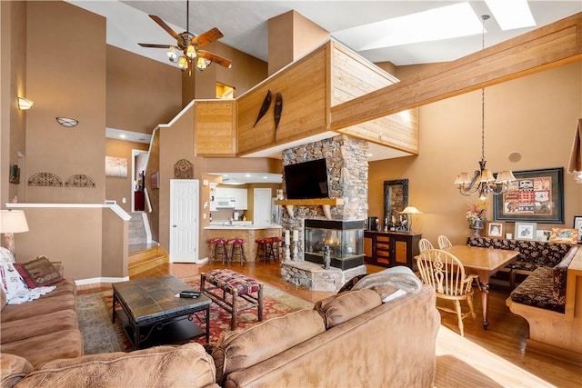 living room with ceiling fan with notable chandelier, a fireplace, high vaulted ceiling, and wood-type flooring