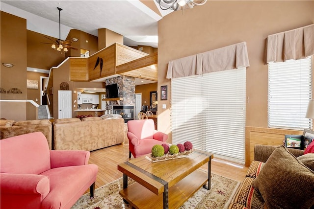 living room with ceiling fan, a fireplace, high vaulted ceiling, and light hardwood / wood-style flooring