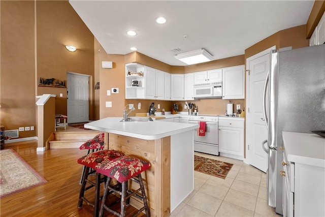 kitchen with a kitchen bar, sink, white cabinetry, kitchen peninsula, and white appliances