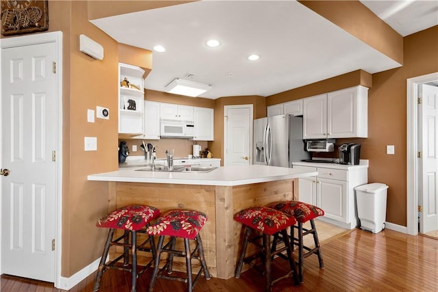 kitchen featuring stainless steel refrigerator with ice dispenser, sink, white cabinetry, a kitchen breakfast bar, and kitchen peninsula