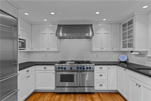 kitchen with white cabinetry, built in appliances, and wall chimney exhaust hood