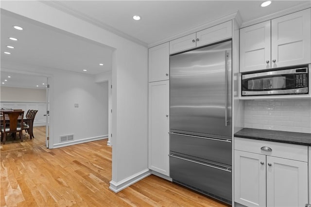 kitchen with stainless steel appliances, ornamental molding, light hardwood / wood-style floors, white cabinets, and decorative backsplash