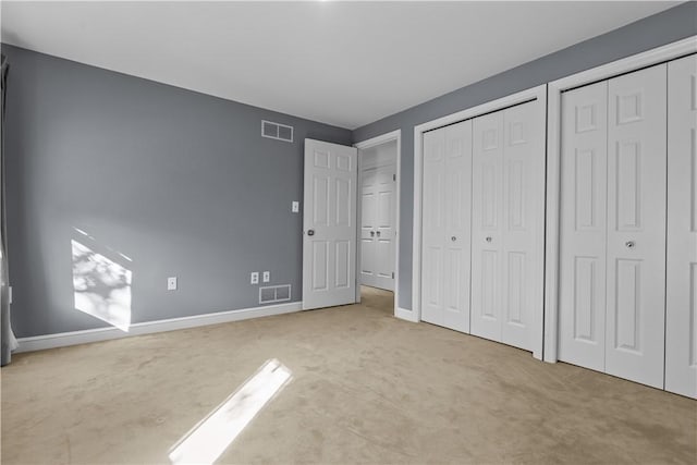 unfurnished bedroom with light colored carpet and two closets